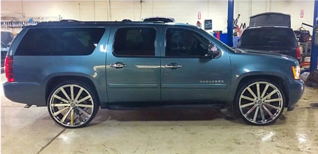 Teal Chevrolet Suburban with oversized chrome custom wheels in Jack's service bay